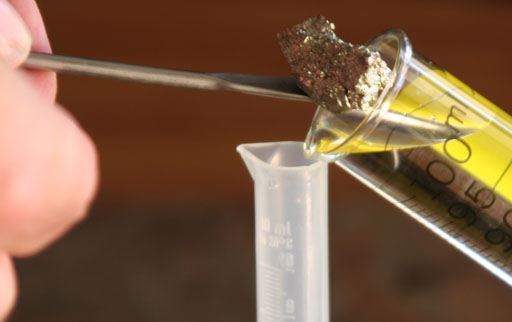 placing gold colored mineral piece into 100 mL graduated cylinder